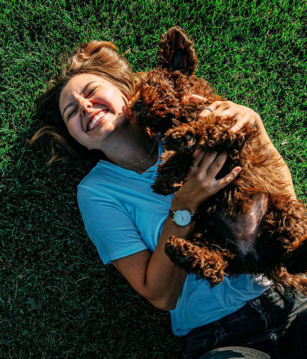Top-down photo fo a girl cuddling a brown dog on the grass